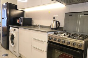 A compact kitchen with a washing machine, a microwave, a kettle, and a gas stove. - Moon River Stylish Studio with Workspace (Dubai)