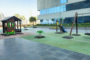 A playground with a wooden playhouse, a swing set, and a slide. - Moon River Stylish Studio with Workspace (Dubai)