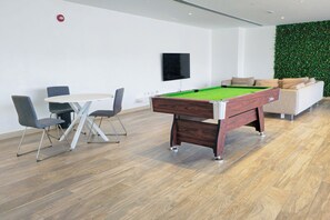 A modern indoor space with a pool table, a flat-screen TV, a sofa, and a green wall. - Moon River Stylish Studio with Workspace (Dubai)