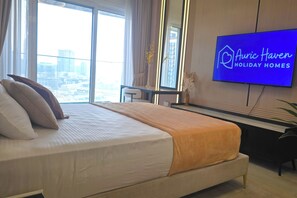 A hotel room with a large bed, a desk, a television, and a view of the city. - Moon River Stylish Studio with Workspace (Dubai)