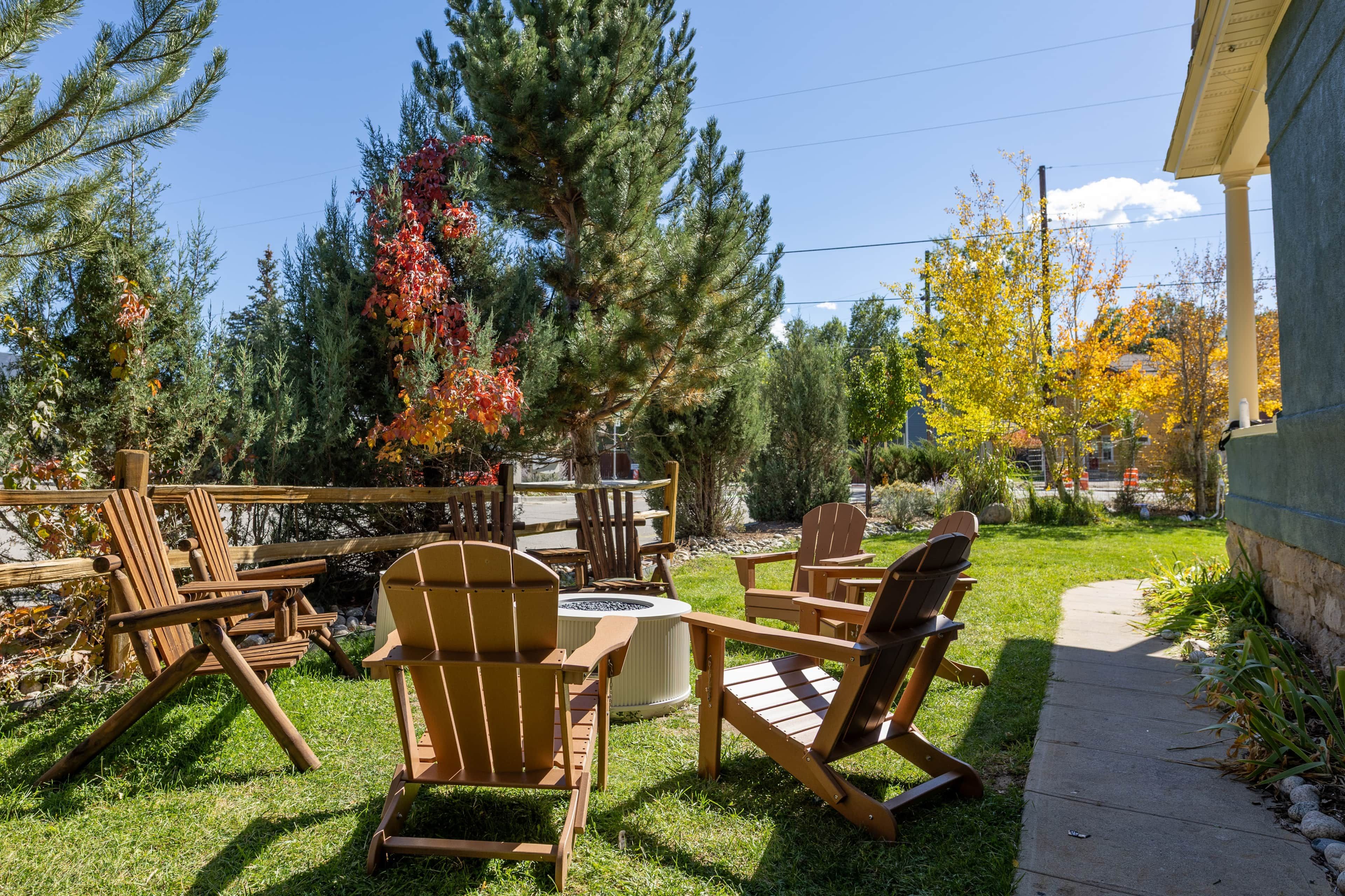 A patio area with wooden Adirondack chairs and a fire pit, surrounded by trees and a stone wall.