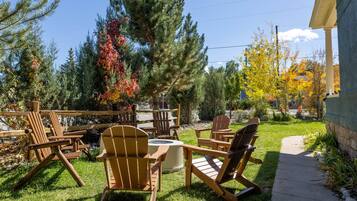 A patio area with wooden Adirondack chairs and a fire pit, surrounded by trees and a stone wall.