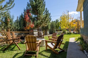 A patio area with wooden Adirondack chairs and a fire pit, surrounded by trees and a stone wall. - The Monarch Ski Room (Salida)