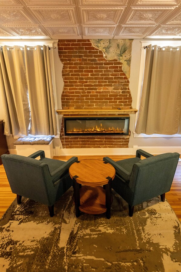 A room with a brick fireplace, two armchairs, a round wooden table, and a patterned rug. - The Monarch Ski Room (Salida)