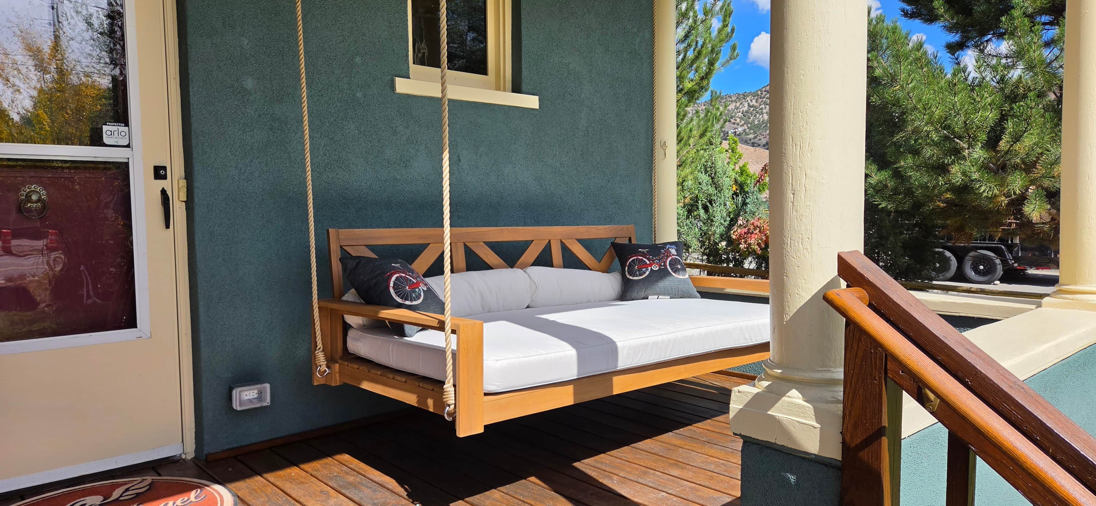 A wooden swing bed with white bedding and two pillows, a window, and a view of trees and a mountain.