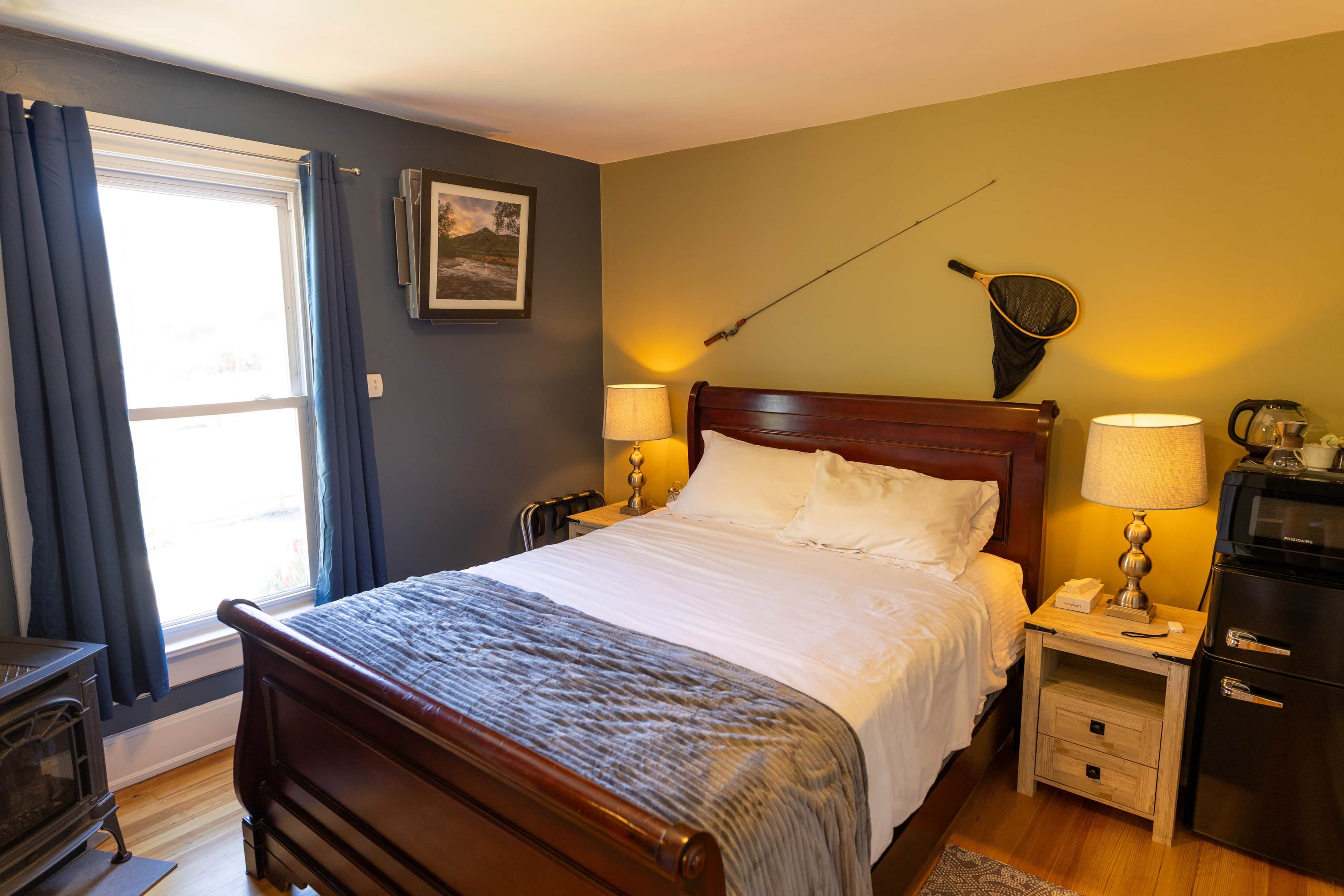 Habitación de hotel con cama, lámparas de noche, mesita, hervidor y un cuadro en la pared.