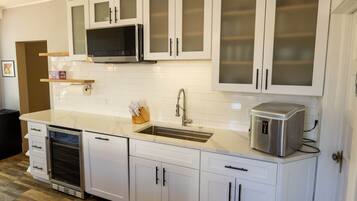 A modern kitchen with white cabinetry, a stainless steel microwave, a built-in oven, a sink, and a coffee maker.