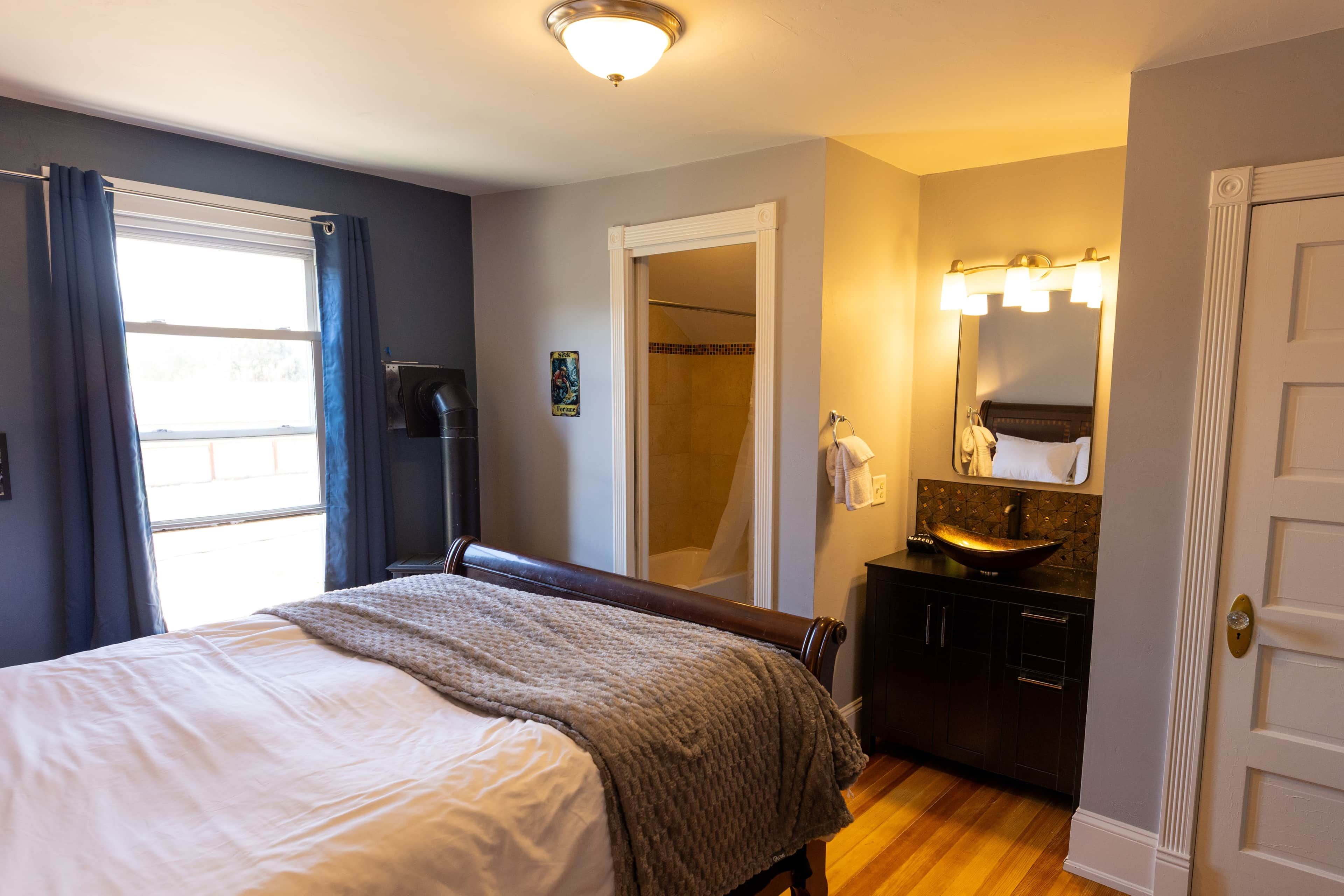 Una habitación de hotel con una cama, un baño con un lavabo y espejo, y una puerta.