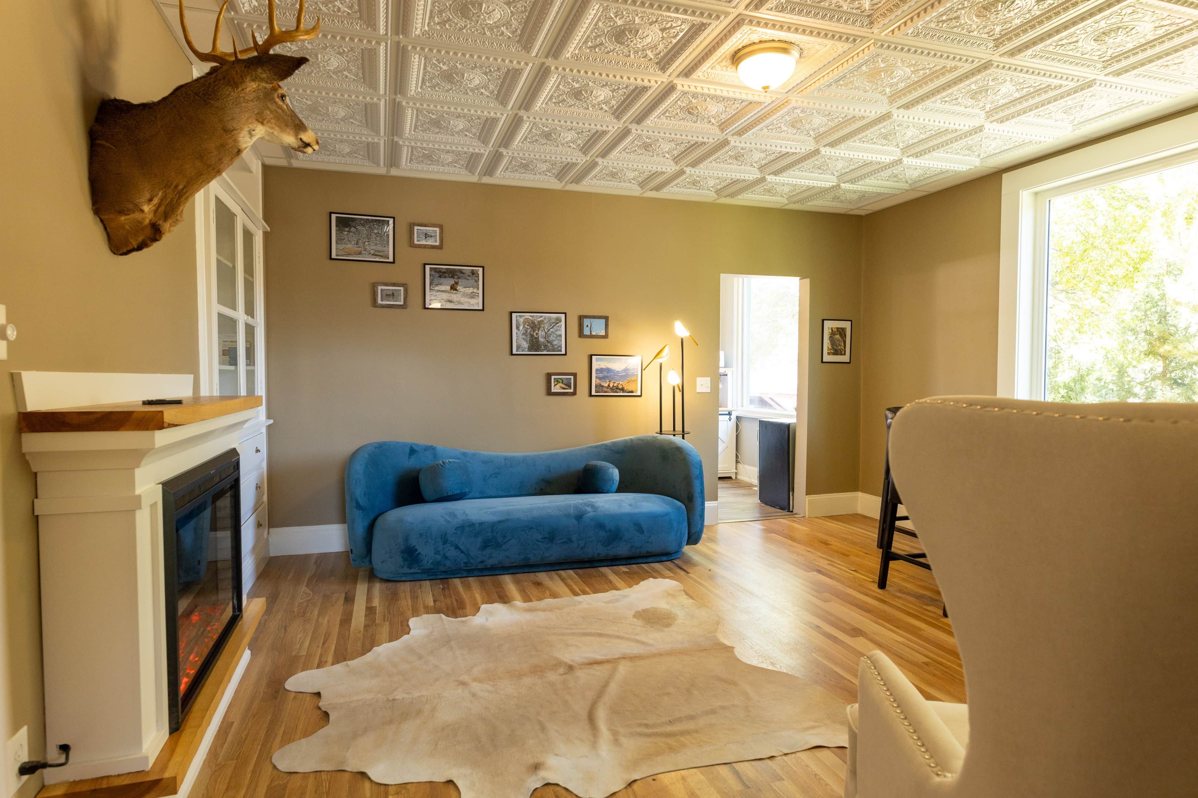Ein Zimmer mit Kamin, einem blauen Sofa, einem Fellteppich und einem Hirschgeweih an der Wand.