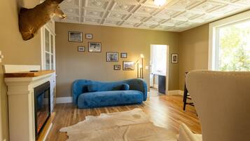 A room with a fireplace, a blue sofa, a fur rug, and a deer head mounted on the wall.