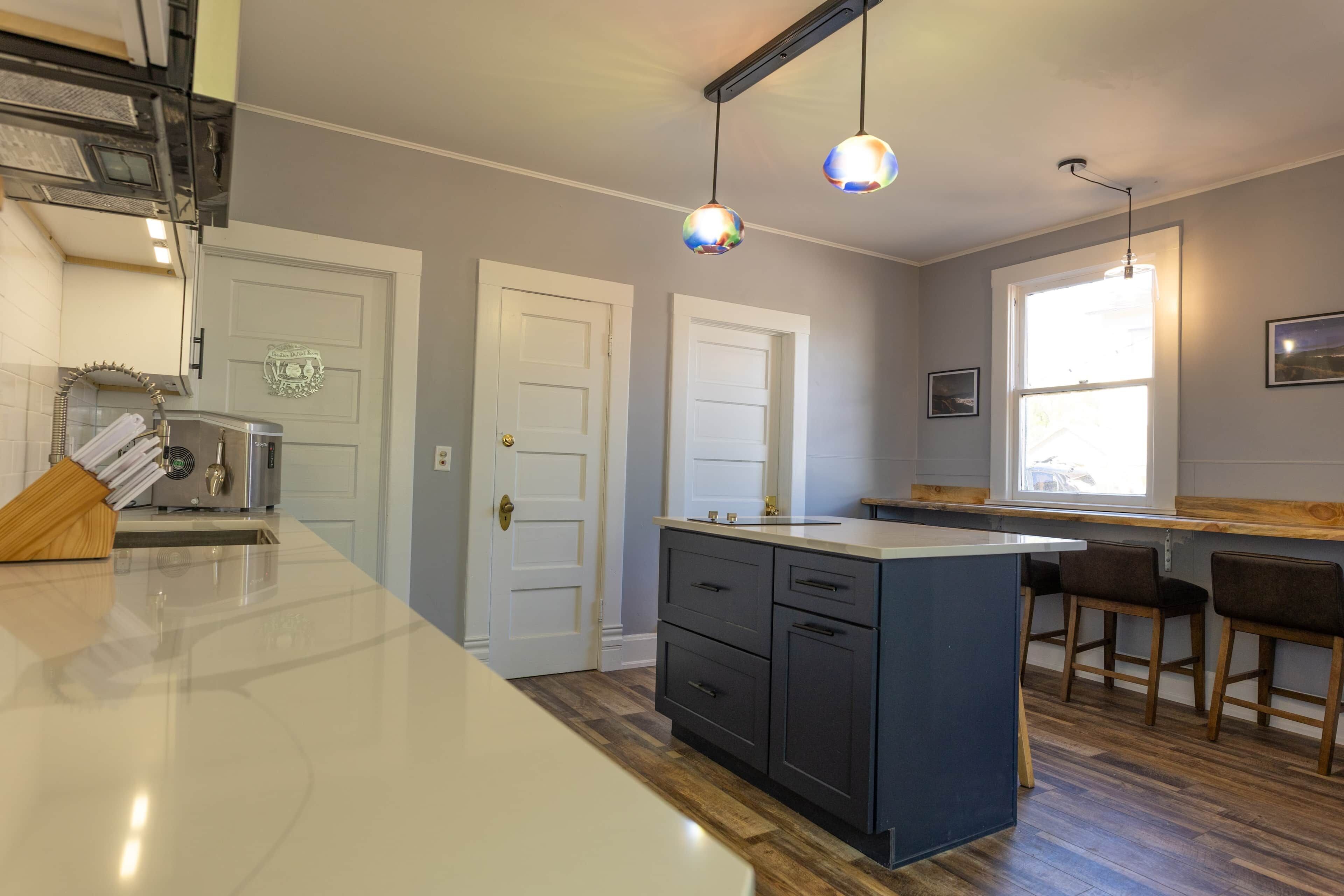 A kitchen with a central island, two pendant lights, a window with a view, and a door with a decorative emblem.