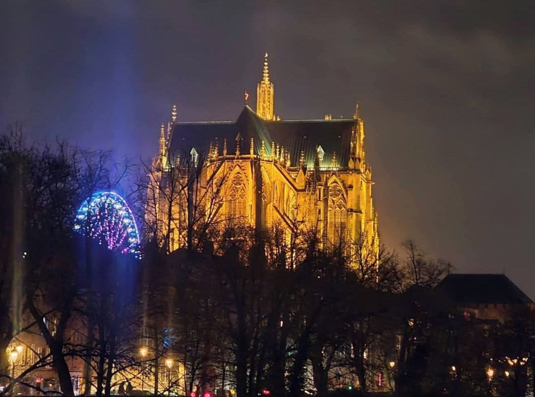 A large, illuminated building with a prominent tower and spire, surrounded by bare trees.