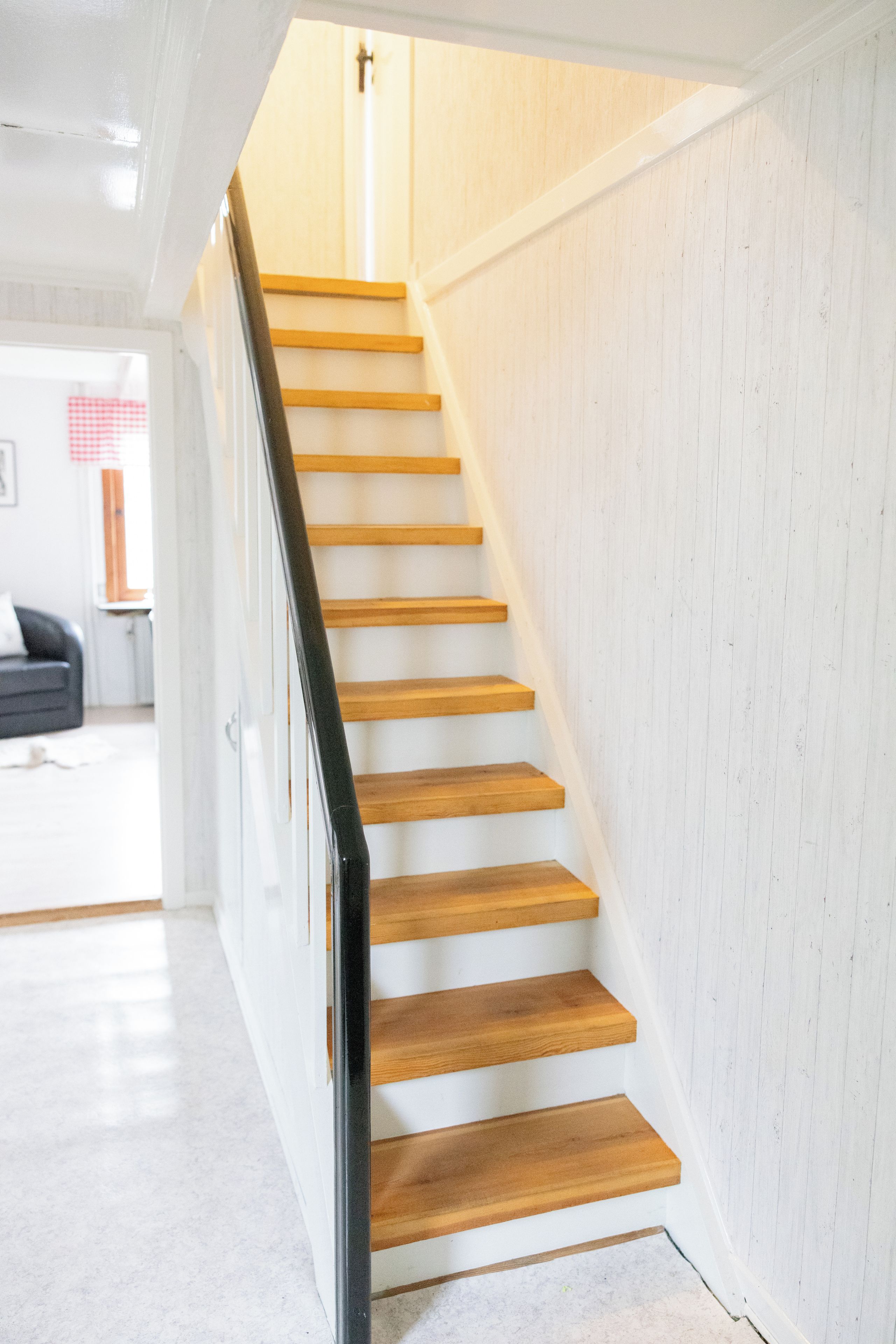 A staircase with wooden steps and a black handrail, leading to a room with white walls and a visible window.