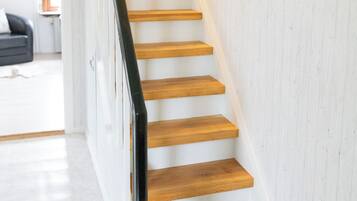 A staircase with wooden steps and a black handrail, leading to a room with white walls and a visible window.