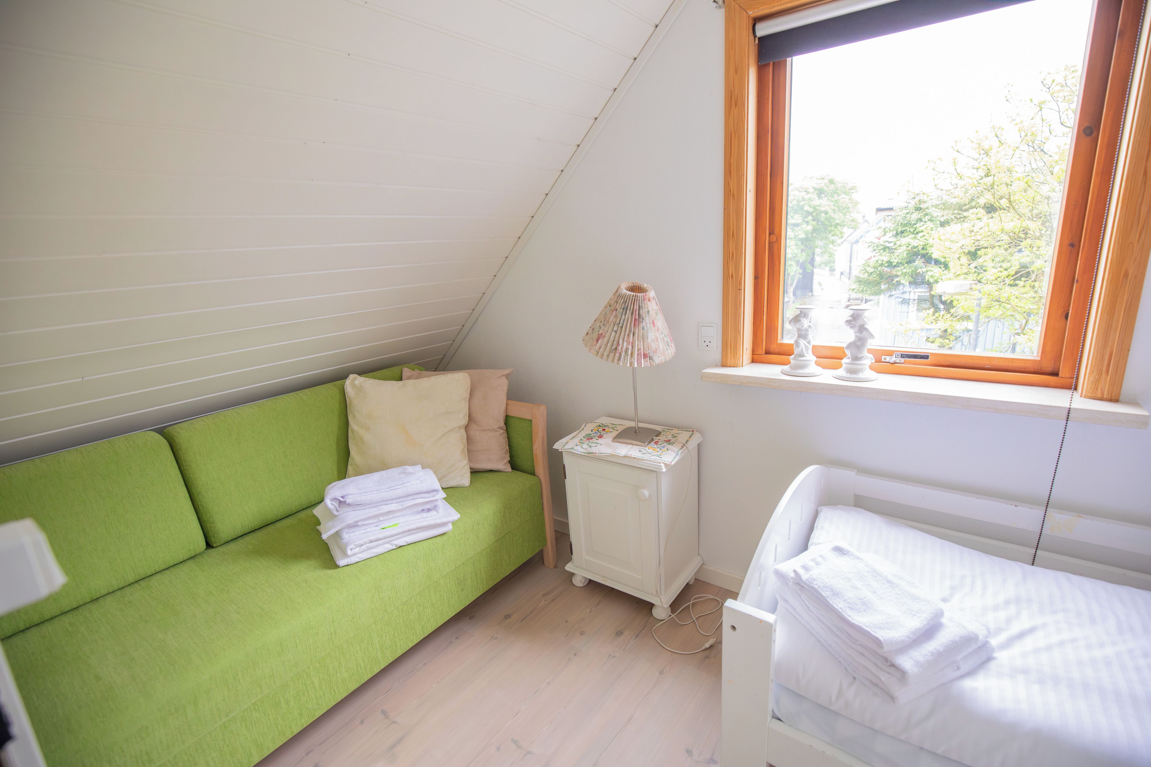 Un alojamiento pequeño y de una sola habitación con sofá verde, mesita de noche blanca, radiador y ventana con vistas a zonas verdes.