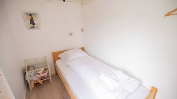 Une petite chambre avec un lit simple, un cadre en bois, un matelas blanc et une table de chevet avec une lampe.