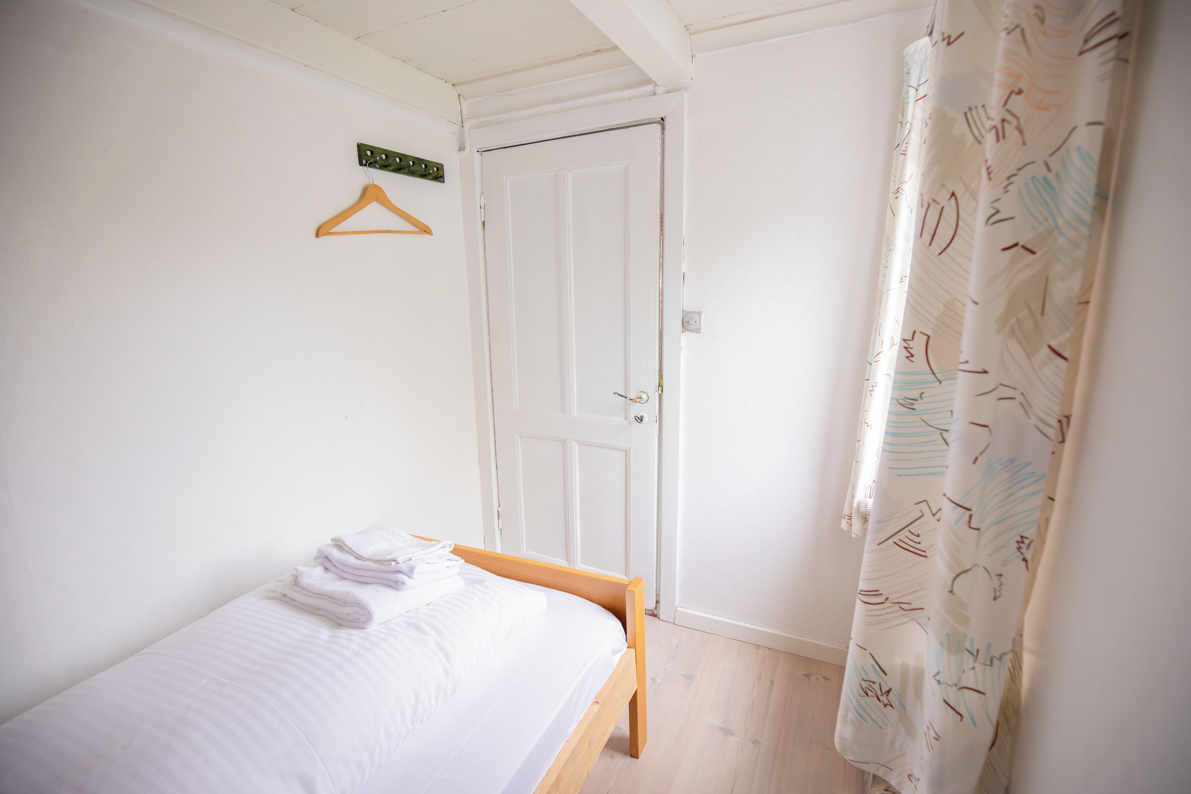 A small, single-bed room with a wooden bed frame, a white wall, and a door with a handle.