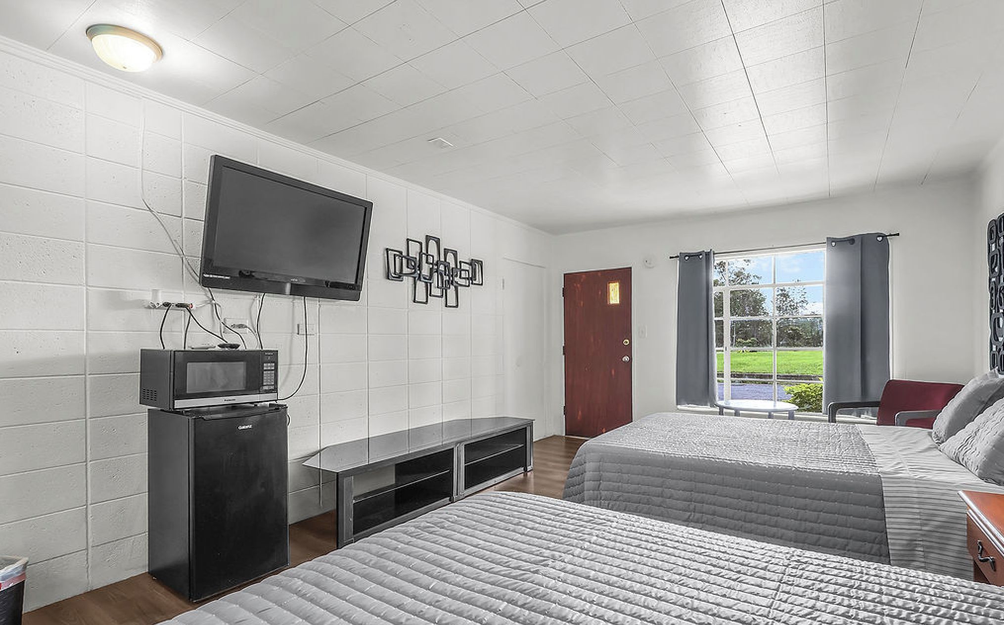 A hotel room with two beds, a television, a microwave, and a door leading to a balcony with a view.