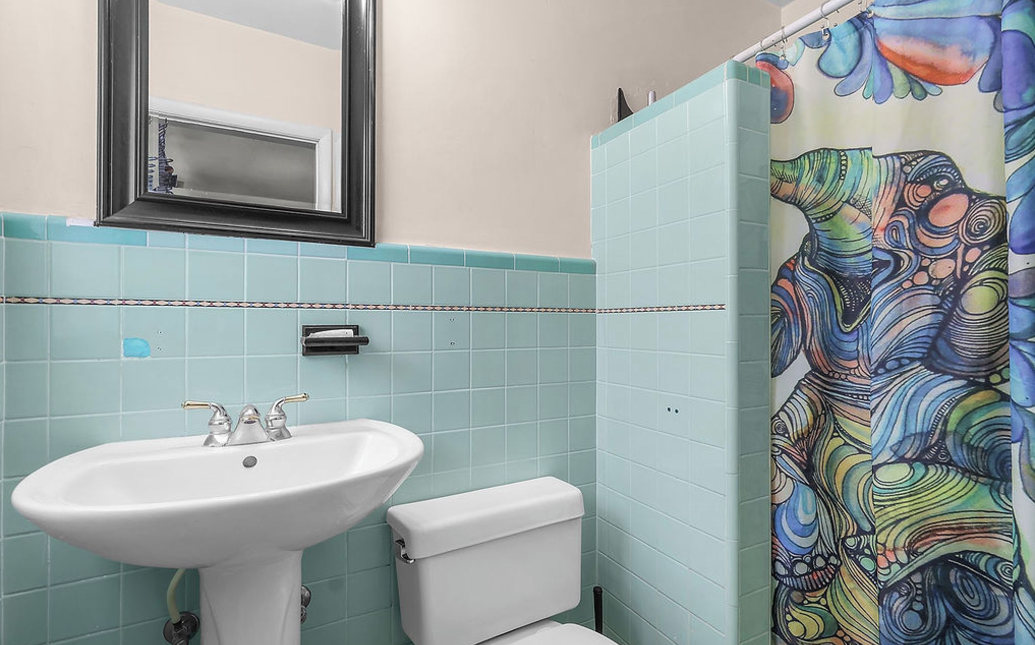 A bathroom with a white sink, a toilet, and a shower curtain with a colorful abstract pattern.