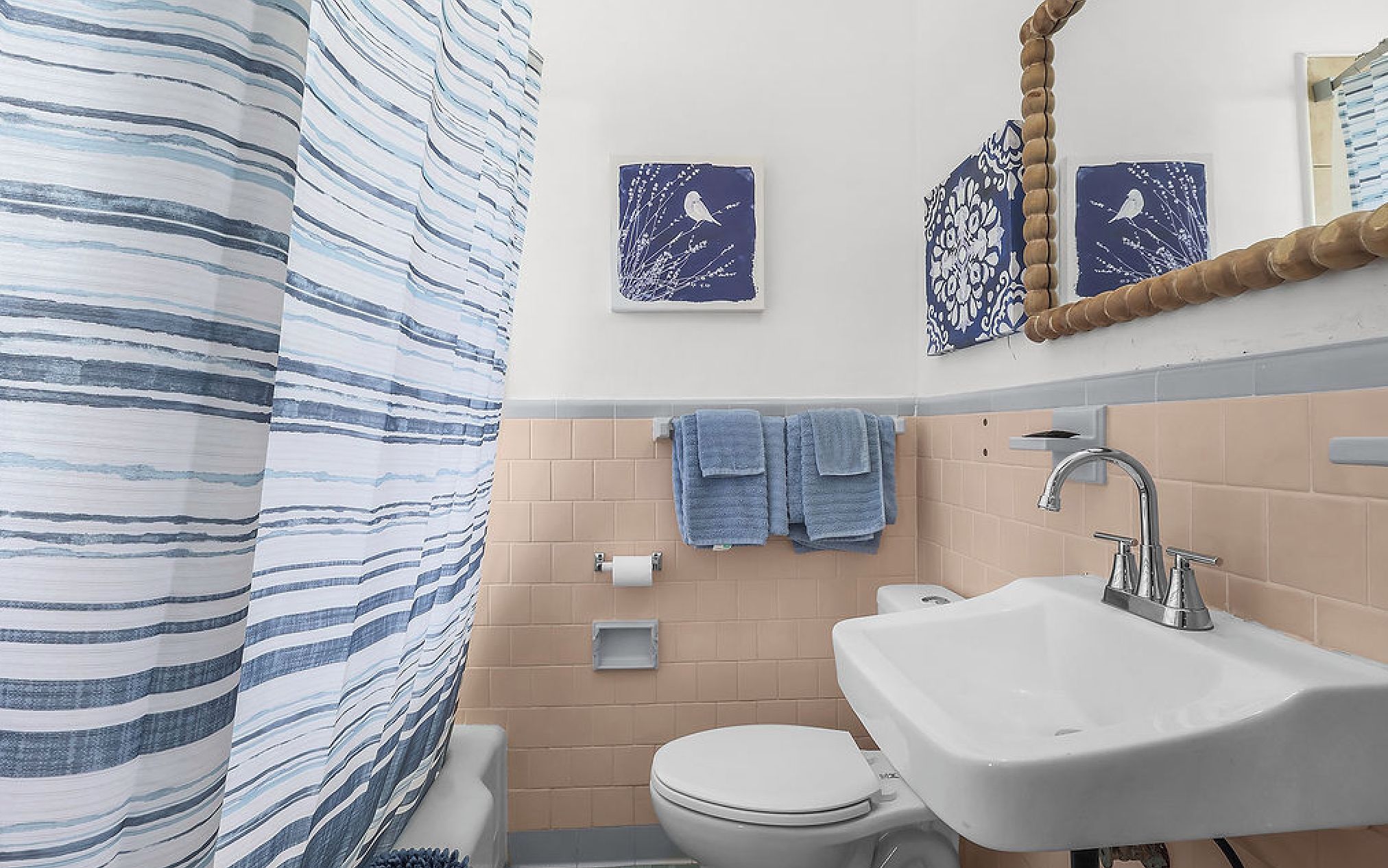 A bathroom with a striped shower curtain, a white sink, a toilet, and two wall-mounted towels.