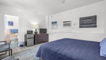A bedroom with a bed, dresser, desk, and a view of the bathroom.