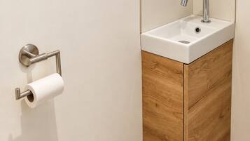 Une salle de bain équipée d’un porte-rouleau de papier toilette, d’un lavabo avec un robinet et d’une poubelle.