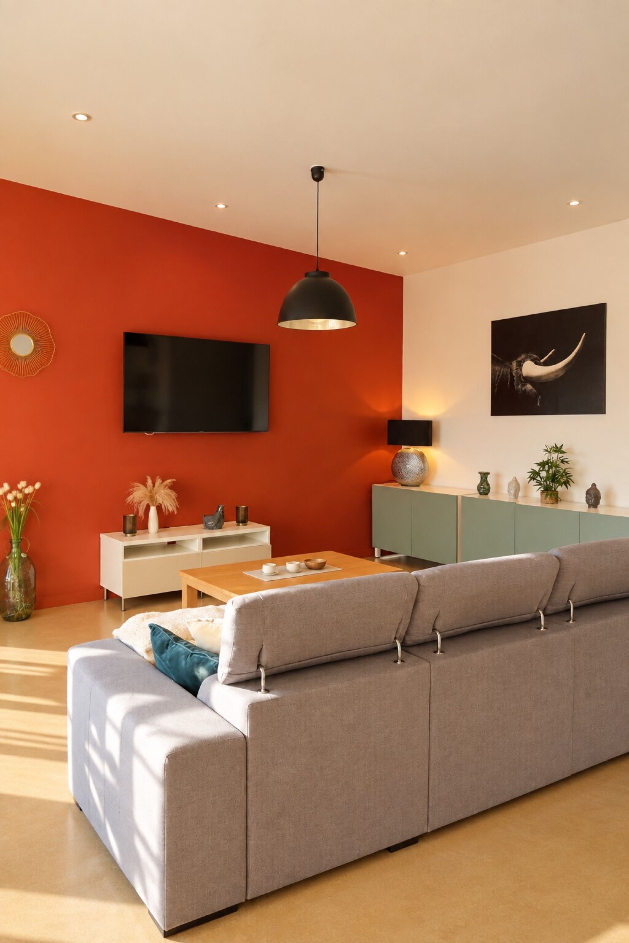 Una sala de estar moderna con un sofá gris, una mesa de centro de madera, un mueble blanco para televisión y una pared decorativa roja.