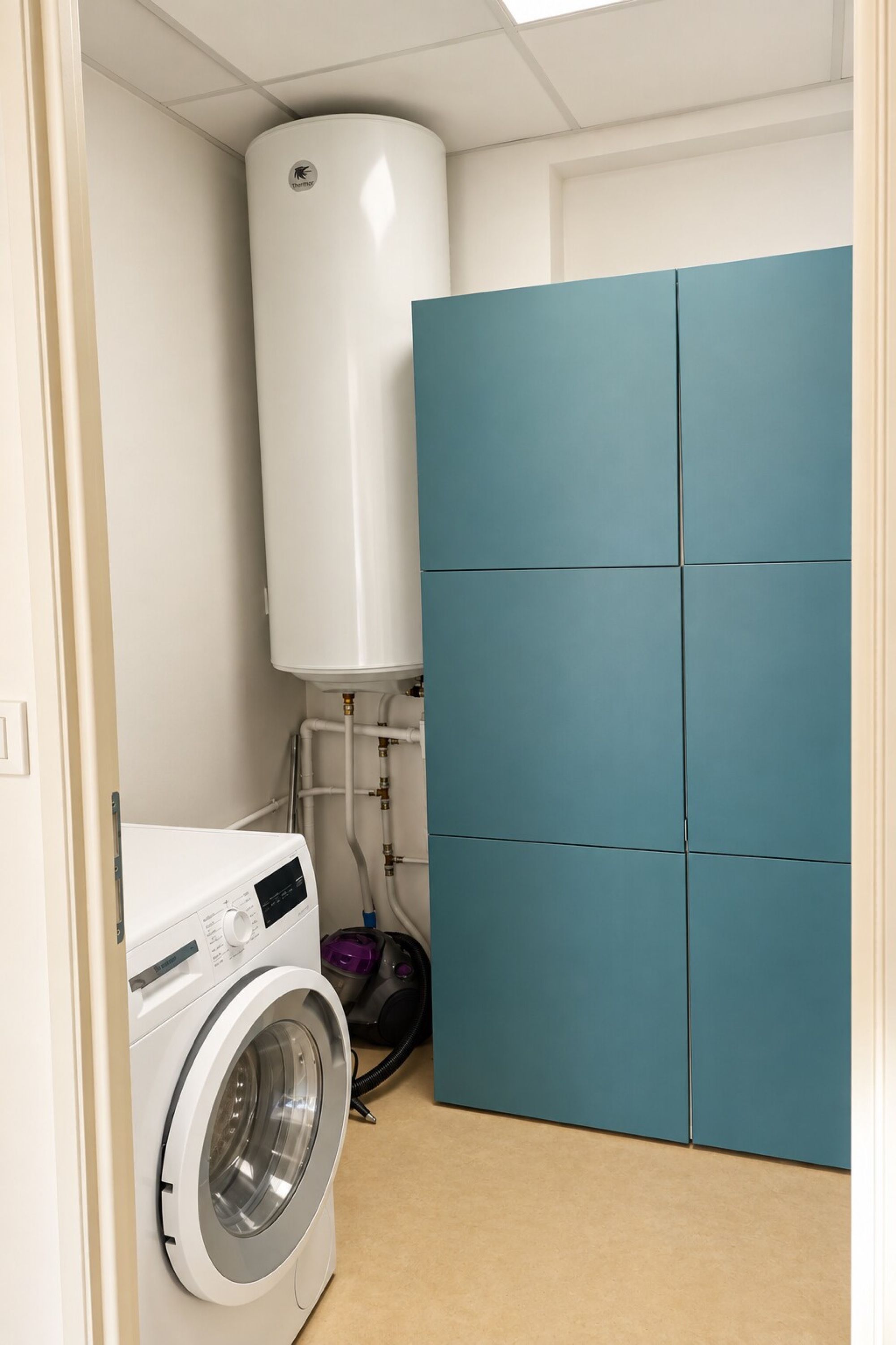 A laundry room with a white washing machine, a water heater, and a blue folding cabinet.