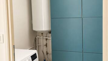 A laundry room with a white washing machine, a water heater, and a blue folding cabinet.