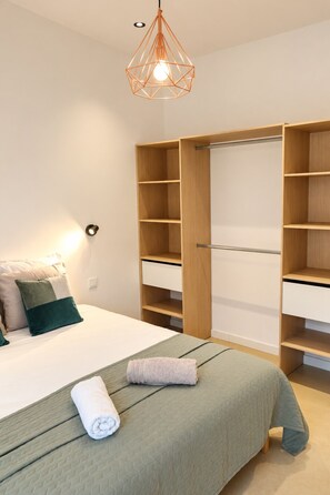 Un dormitorio con cama, mesita de noche, armario y lámpara colgante.