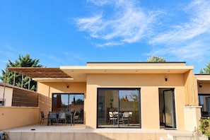 Une maison moderne dotée d’un patio, d’un coin repas et d’une grande porte-fenêtre coulissante.