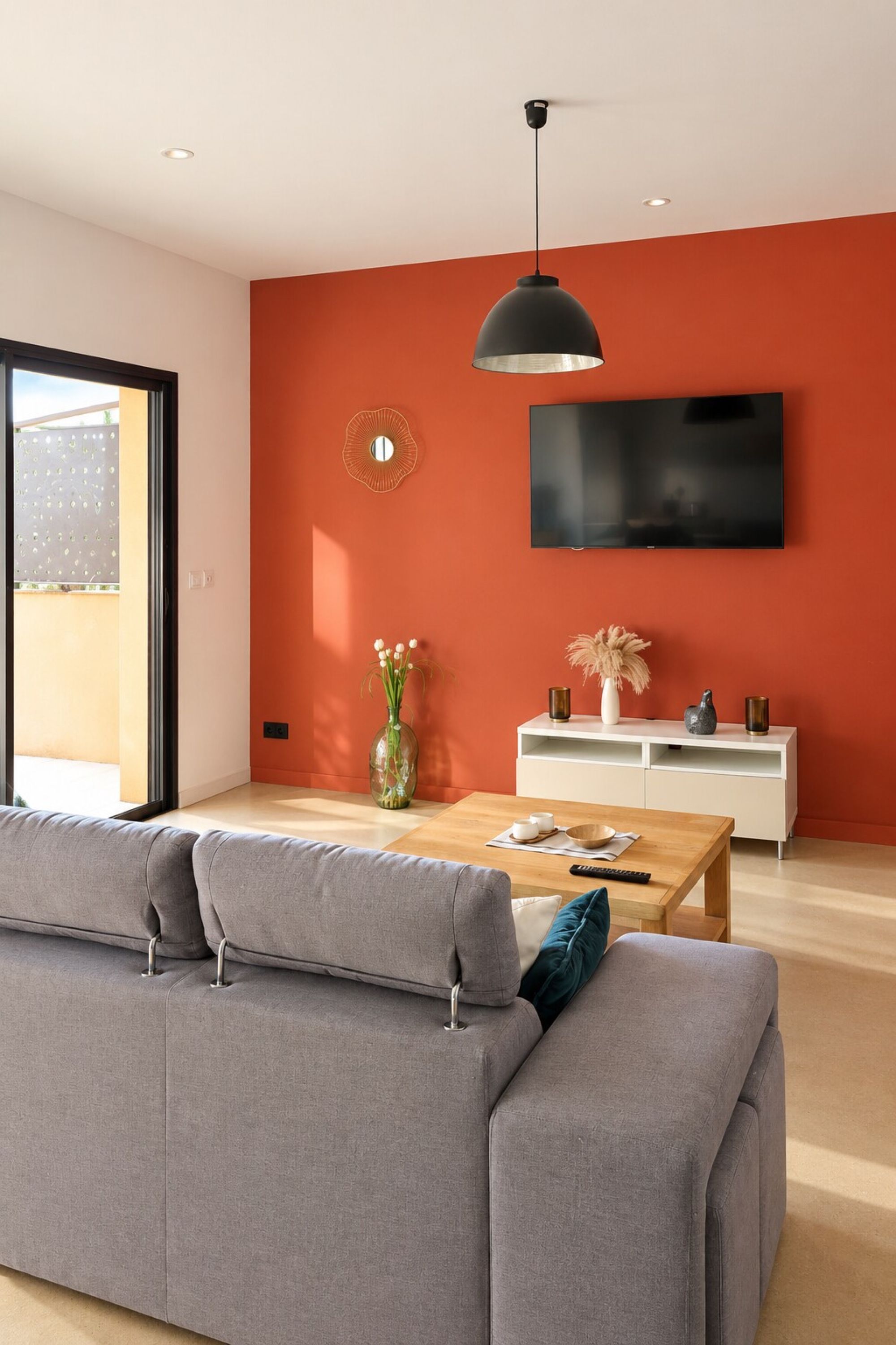 Un salon moderne avec un canapé gris, une table basse en bois, un meuble TV blanc et un mur d’accent rouge.