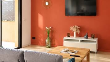 Un salon moderne avec un canapé gris, une table basse en bois, un meuble TV blanc et un mur d’accent rouge.