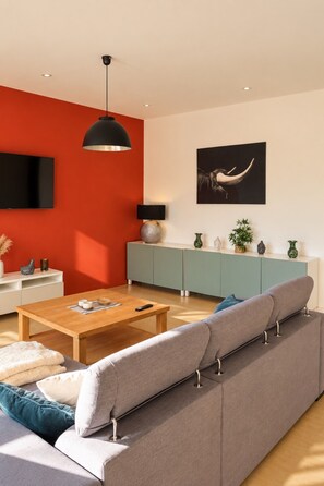 Una sala de estar moderna con un sofá gris, una mesa de centro de madera y una pared de acento roja.