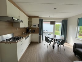 Ett modernt kök med gasspis, mikrovågsugn och kaffebryggare, som leder vidare till en matplats med bord och stolar.