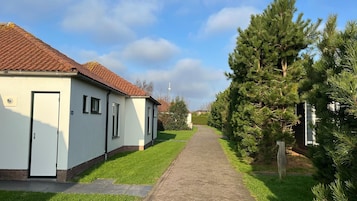 En stig som leder fram till en byggnad med ett tak täckt av takpannor och en dörr, omgiven av gräs och träd.