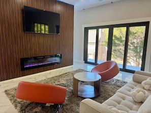 Un salon moderne avec un téléviseur à écran plat fixé à un mur en bois, une cheminée avec une façade en verre et une grande porte-fenêtre coulissante donnant sur un espace extérieur.