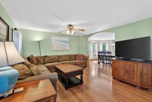Ein Wohnzimmer mit einer Eckcouch, einem Couchtisch, einem Fernseher und einem Essbereich mit Stühlen und Tisch.