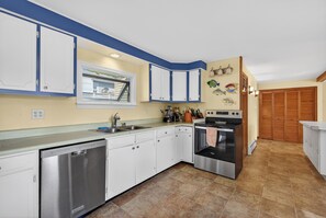 A kitchen with white cabinets, a dishwasher, an oven, and a window with a view of a balcony. - Beautiful 5-bedroom house with AC 5-min walk to Old Orchard Beach (Old Orchard Beach)