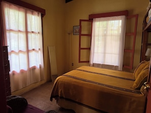 A room with a bed, a window with curtains, a bedside table, and a lamp.