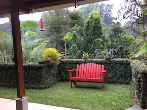 A red bench in a lush garden with various plants and a red hanging light fixture.
