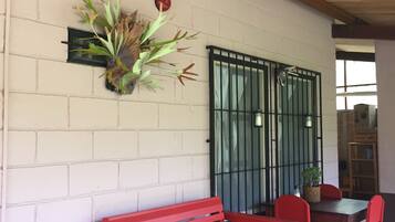 A red bench and chairs in a covered outdoor area with a brick wall, a metal gate, and a potted plant.