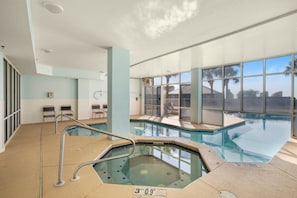 Ein Hallenbad mit Whirlpool, großen Glaswänden und Blick auf Palmen.