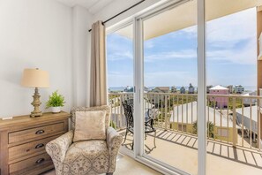 A balcony with a view of a coastal area, a chair, a lamp, and a wooden dresser. - The Dunes 🏖️ Walk to Beach with Indoor + Outdoor Pools + Hot Tub (Fort Morgan)