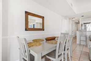A dining area with a white table, four chairs, and a wooden mirror on the wall. - The Dunes 🏖️ Walk to Beach with Indoor + Outdoor Pools + Hot Tub (Fort Morgan)