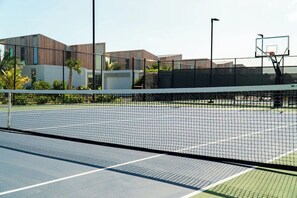 Cancha de tennis a l'aire lliure amb una xarxa, envoltada per una tanca i edificis al fons.