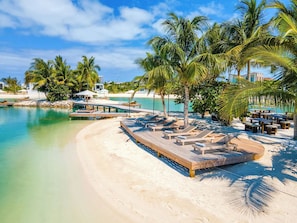 A beach resort with a wooden deck, lounge chairs, and palm trees.