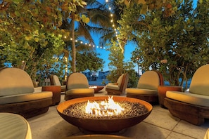 An outdoor seating area with a fire pit, lounge chairs, and string lights.