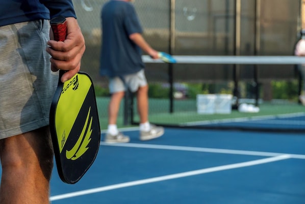 A tennis court with a net in the center, a person holding a tennis racket, and another person in the background.