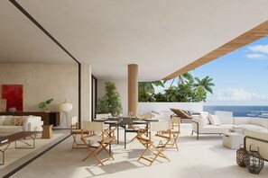 Un salon moderne avec un coin repas, une grande fenêtre donnant sur un paysage tropical et une vue sur l’océan.